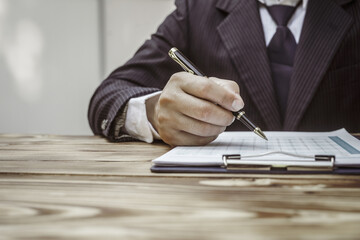 A businessman in a formal suit signs a contract, hands close up, highlighting financial terms like...