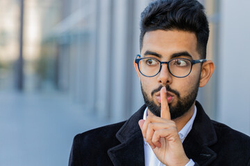 Shh be quiet please. Indian businessman presses index finger to lips makes silence hush gesture...