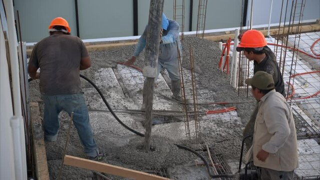 Slow motion of a group of mexican latin construction workers pouring fresh concrete with a boom pump to create the slab of a house in Mexico