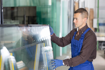 Experienced male glazier controlling quality of sheet glass in workroom