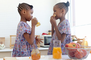 African twin girl sister with curly hair braid African hairstyle eat bread toast with jam and drink...