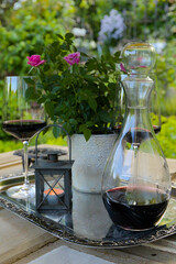 Glass wine carafe with red wine on an antique metal tray with glasses filled with red wine, a pink...
