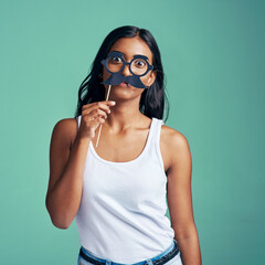 Woman, studio and party prop on face, surprised and comic with holding mask for humorous or comedy. Photo booth, portrait and green background, silly and creative fun with Indian female person