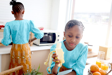 Twin sister girl with curly hair braid African hairstyle have meal together in kitchen. Happy kid...