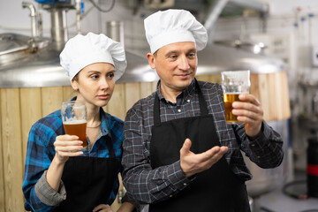 Brewers man and woman is standing with glasses for beer on his workplace indoor