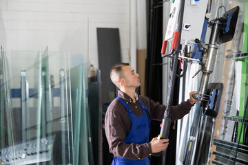 Focused professional operator maneuvering large glass sheets with vacuum lifter in industrial...