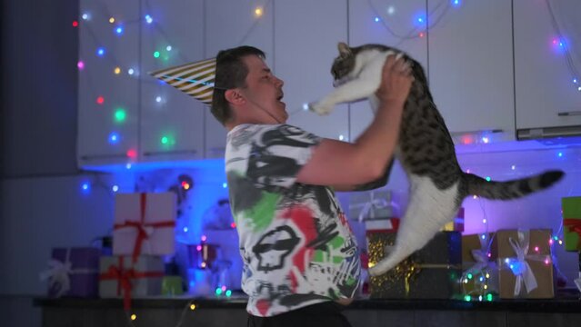 Loser man celebrates his birthday alone with his best friend cat dancing in the kitchen in a festive atmosphere prepared for a party to which no one came.