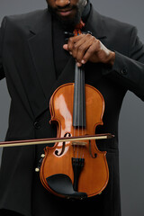 An elegant African American man in a suit holding a violin on a neutral gray background