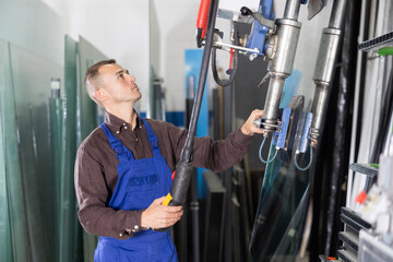 Focused professional operator maneuvering large glass sheets with vacuum lifter in industrial...