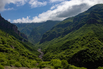 River landscape between the mountain slopes. Beautiful green cloudy landscape of mountains and blue sky