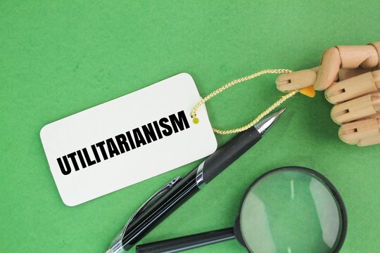 magnifying glass, pen and paper tag with the word Utilitarianism. Utilitarianism is a theory of morality that advocates actions that foster happiness