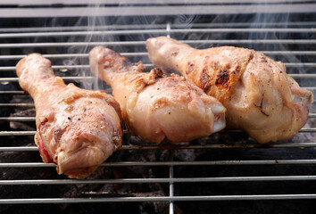Close up of charcoal grill with three cooked chicken legs on grate.