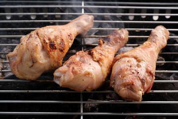 Cooked chicken legs cooking on charcoal grill.
