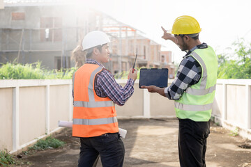 Foreman, engineer or architect wearing hard hat holds laptop and blueprints to check details about real estate construction in Construction area of ​​an unfinished building