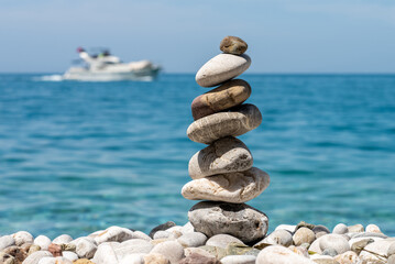 Stones stacked in a pyramid on a sunny day on a pebble beach, blurred background with a ship. Mediterranean Sea.