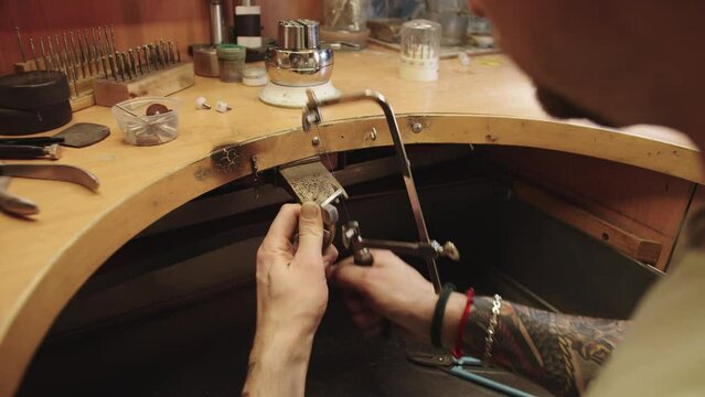 A man is working on a piece of jewelry, using a tool to cut a piece of metal