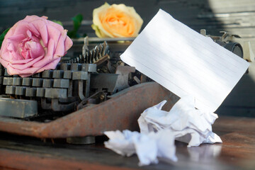 Blank torn paper with pink and yellow roses on an old rusty typewriter vintage background on a messy table. Copy space for your text message. Life inspirational backgrounds.