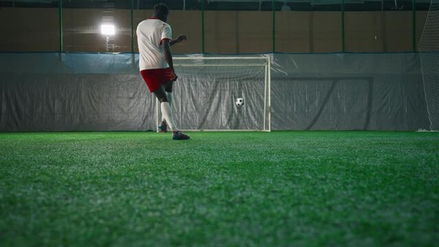 Black soccer player exercising penalty in training hall, scoring goal, back view