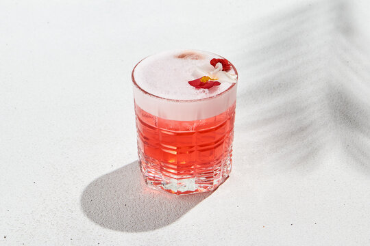 Aesthetic composition with alcoholic cocktail with flowers on white background. Pomegranate fizz in minimal style. Grapefruit sour with gin. Alcoholic beverage in elegant style with palm shadows.
