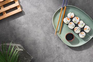 Modern japanese food concept. Maki sushi on ceramic plate with soy sauce and chopsticks on stone...