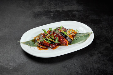 Delicatessen appetizer - grilled octopus with eggplant in teriyaki sauce. Boiled octopus tentacle and vegetables in pan asian style. Salad with octopus and eggplant in miso sauce on black table.
