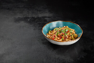 Traditional asian fried noodles with chicken and vegetables on dark background. Udon noodles with chicken on wok with sesame and green onion. Stir-fried udon with meat and vegetables on wok.