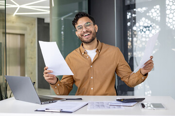 Happy businessman celebrating success at the desk with paperwork in a modern office