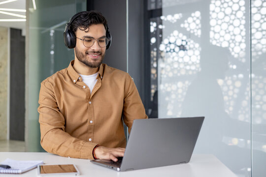 Smiling man with headphones working on a laptop in a modern office - Powered by Adobe