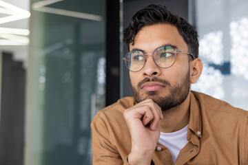 Thoughtful young man with glasses contemplating an idea indoors