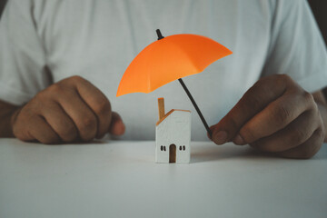 Man holding orange umbrella protection home symbolizes holistic insurance protection for family,...