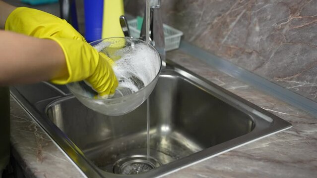 Close-up - a woman in rubber yellow gloves washing and washing dishes in the kitchen under a faucet. Washing dishes in the kitchen.