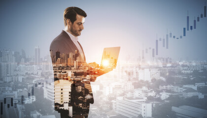 Attractive young european businessman with laptop standing on blurry airy city background with mock...