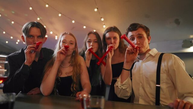 People celebrating b-day, blowing noisemakers whistles, congratulation party. Portrait of happy five best friends cheering and greeting, merry birthday party, gathering in festival in nightclub