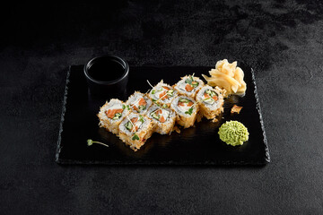Bonito roll with tuna flakes and salmon inside, served on a black slate with soy sauce, wasabi, and ginger