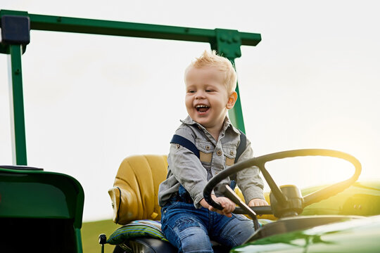 Laughing, child and driving tractor on farm in countryside for learning agriculture outdoor in nature. Funny kid, farmer and play on steering wheel for growth, development and happy on summer fielda