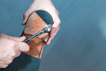 Footwear Repairing. Hands of Professional Shoemaker in Apron Repairing Sole of Black Polished...