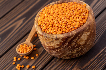Photo of red lentils in wooden bowl with wooden measuring cup on wooden background.  Healthy lifestyle. Vegetarian and vegan diet.