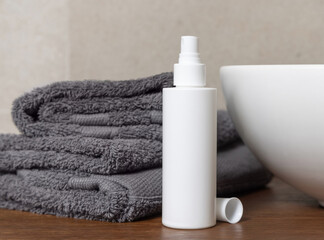 White cosmetic bottle near grey folded towels on basin on wooden countertop in bath, mockup