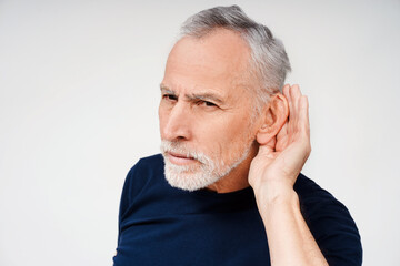 Portrait of senior gray-haired man having hearing problems posing in studio, isolated