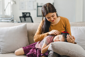 Mother lulls child to sleep. Mother gently strokes her daughters hair as the child rests her head on a pillow on the sofa.