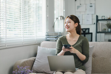 Young asian businesswoman working from home on a laptop while chatting on phone in a bright living room.