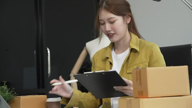 A young Asian businesswoman efficiently manages SMEs, utilizing her desk, tablet, laptop to handle online orders and live streams, showcasing entrepreneurial prowess in the dynamic market landscape.