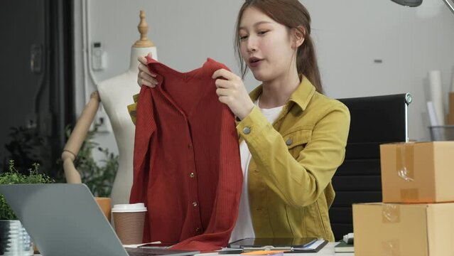 A young Asian businesswoman efficiently manages SMEs, utilizing her desk, tablet, laptop to handle online orders and live streams, showcasing entrepreneurial prowess in the dynamic market landscape.