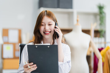 A young Asian businesswoman efficiently manages SMEs, utilizing her desk, tablet, laptop to handle...