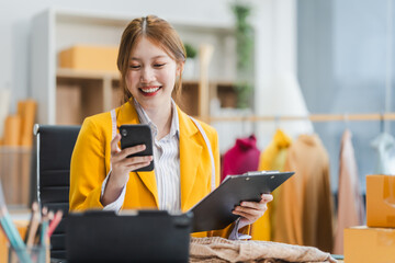 A young Asian businesswoman efficiently manages SMEs, utilizing her desk, tablet, laptop to handle...