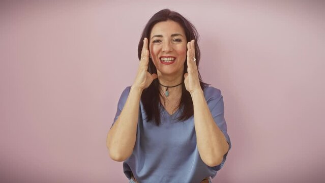 Frustrated middle-aged hispanic woman goes mad, standing yelling with aggression, arms flailing wildly over an isolated pink background. feel the raw emotion!