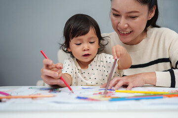 toddler baby training to drawing with colored pencil with mother helping on table