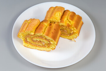 Slices of lemon Swiss roll on dish on gray background