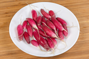 Fresh red radish oblong shape on dish on wooden surface