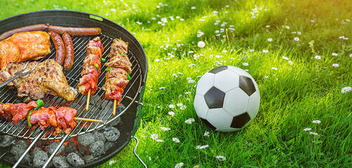  Delicious grilled meat with vegetables sizzling over the coals on barbecue with a soccer ball on...